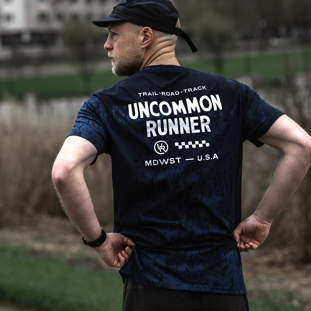 Image of a man wearing a navy t-shirt with the words "Uncommon Runner - Trail Road Track" displayed prominently across the back.