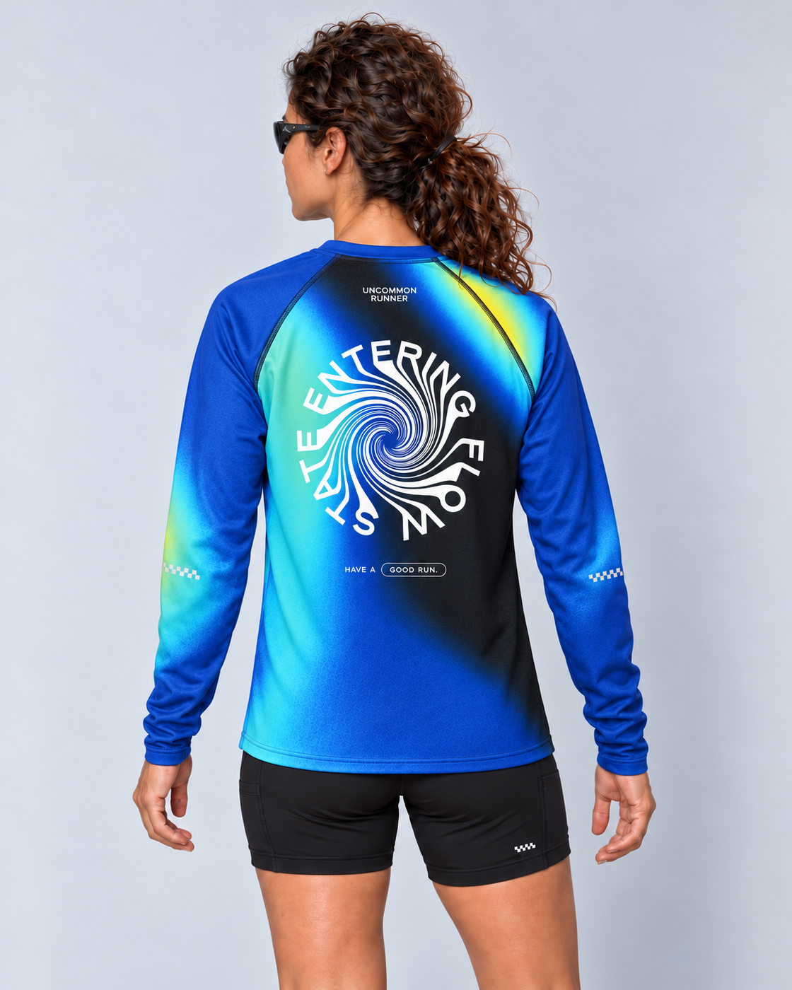 Back studio view of a female model wearing the Entering Flow State long-sleeve TempoTech running tee with black Shift-5 shorts