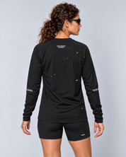 Back studio view of a female model wearing the black and yellow Keep Running Weird long-sleeve TempoTech running tee with black Shift-5 shorts