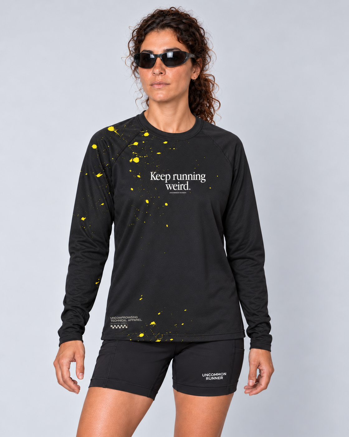 Front studio view of a female model wearing the black and yellow Keep Running Weird long-sleeve TempoTech running tee with black Shift-5 shorts