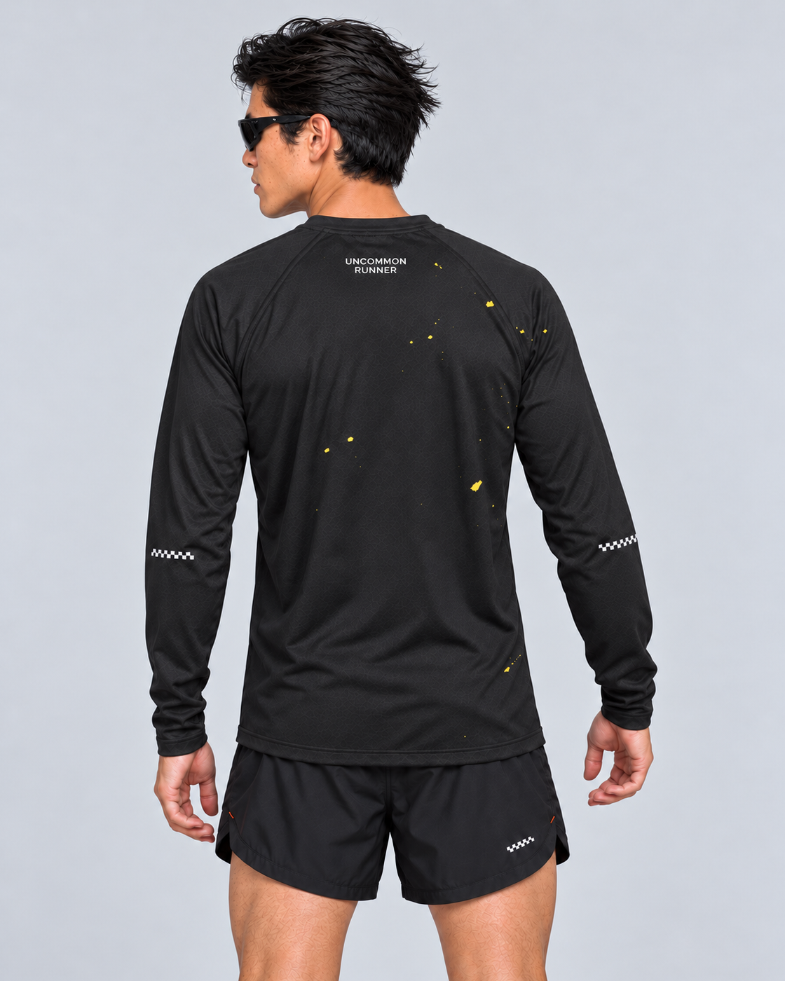 Back studio view of a male model wearing the black and yellow Keep Running Weird long-sleeve TempoTech running tee with black Phanto-3 race shorts