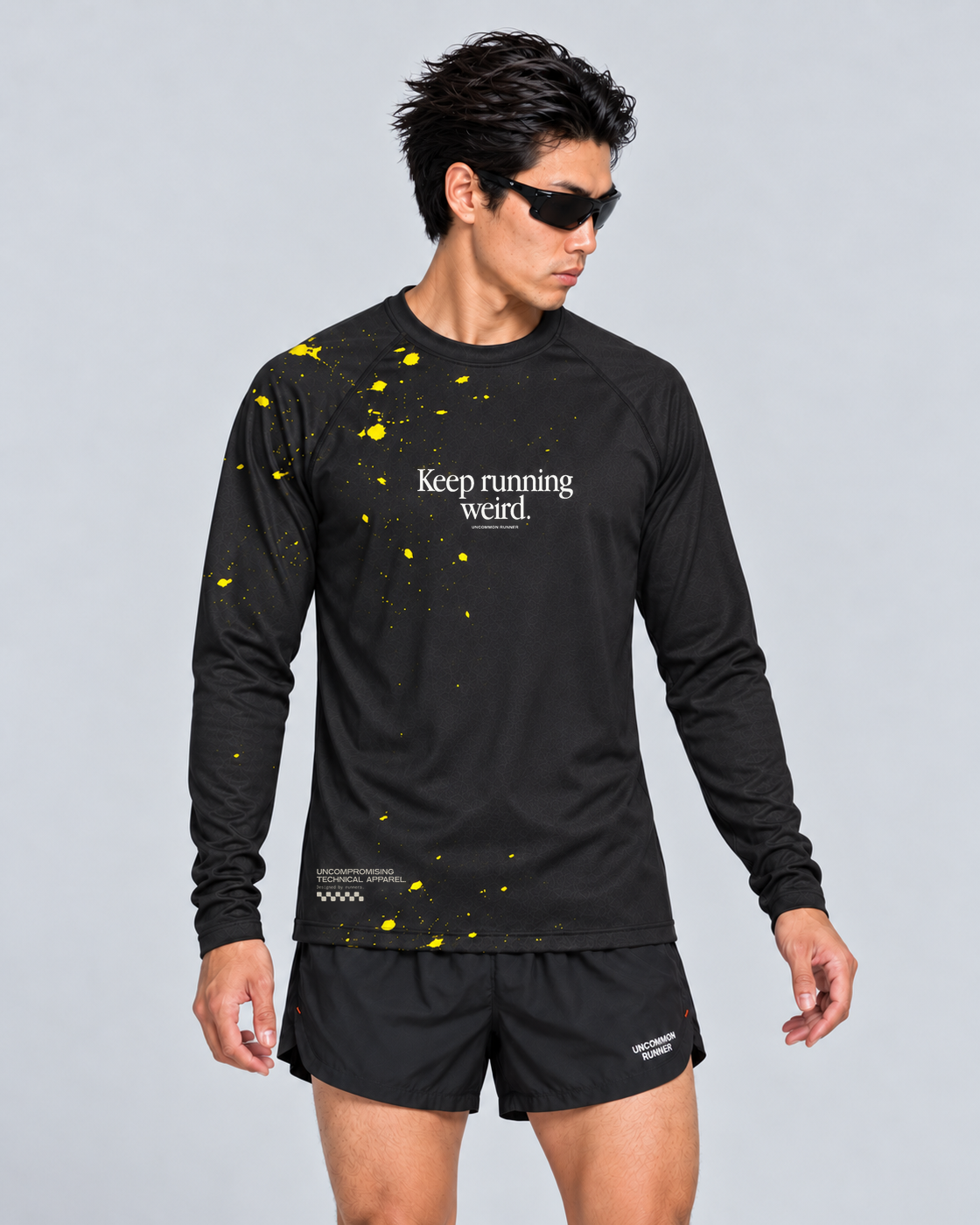 Front studio view of a male model wearing the black and yellow Keep Running Weird long-sleeve TempoTech running tee with black Phanto-3 race shorts