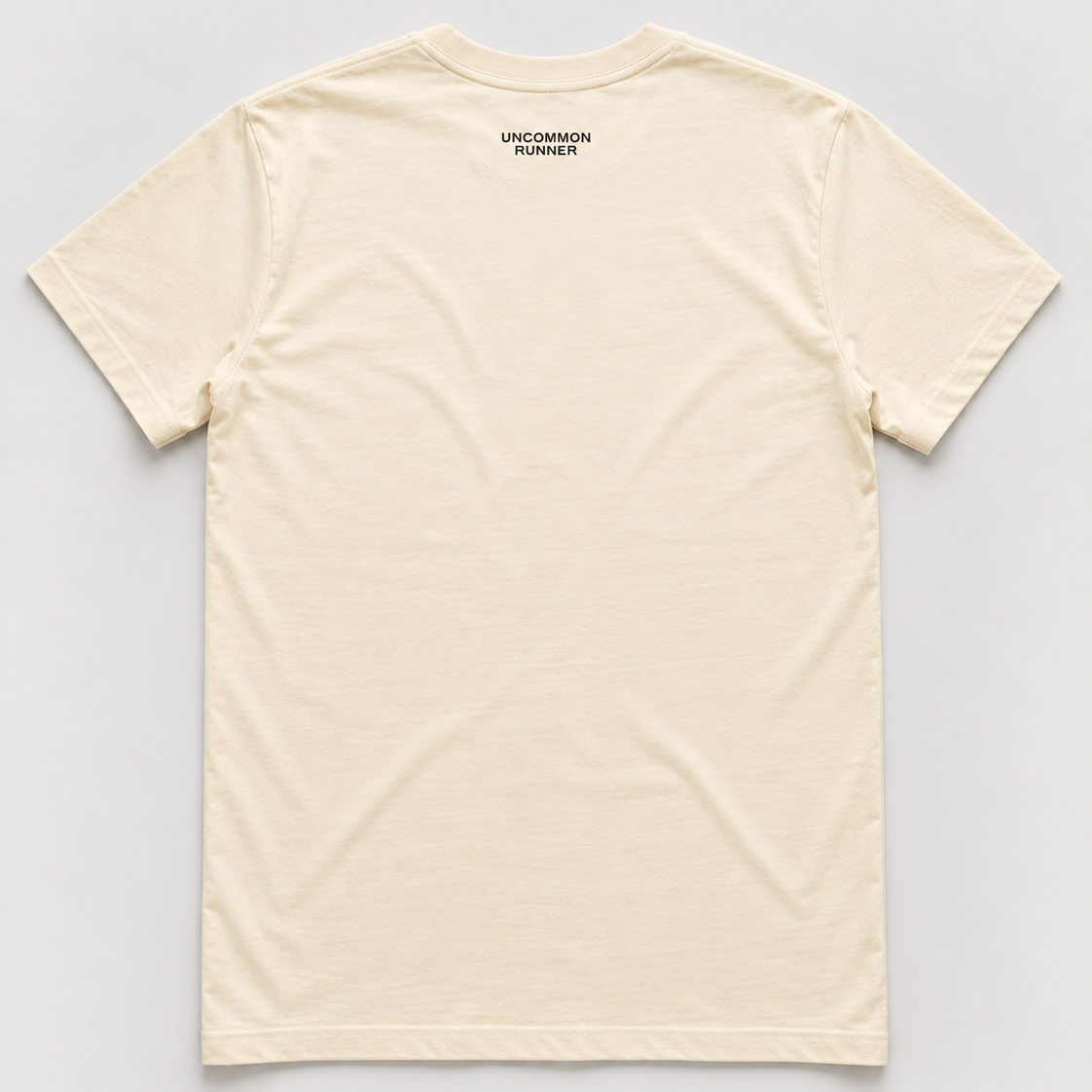 Back mockup of Uncommon Runner Kicks cotton tee in ecru with small black Uncommon Runner neck logo.