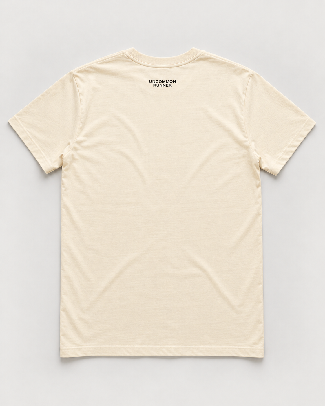 Back mockup of Uncommon Runner Kicks cotton tee in ecru with small black Uncommon Runner neck logo.