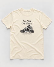 Front mockup of Uncommon Runner Kicks cotton tee in ecru, with See You Out There text and black-and-white shoe graphic.